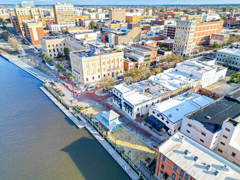 Aerial view of North Water Street along the Cape Fear River with historic buildings, a wooden boardwalk, and urban infrastructure in Wilmington, North Carolina, United States.