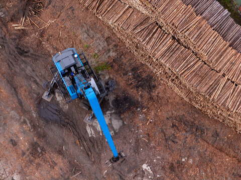 Aerial view of a blue forestry machine operating in a lumber yard next to large stacks of logs in Gdansk, Poland.