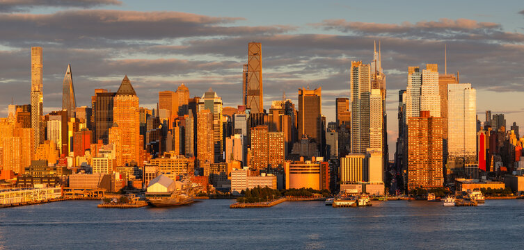 UNITED STATES, NEW YORK CITY, MANHATTAN. GOLDEN HOUR VIEW OF MIDTOWN SKYLINE ALONG THE HUDSON RIVER. SKYSCRAPERS AND URBAN WATERFRONT CITYSCAPE IN WARM SUNSET LIGHT