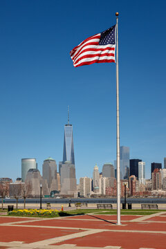 UNITED STATES, NEW YORK CITY, MANHATTAN, FINANCIAL DISTRICT. AMERICAN FLAG STANDING TALL IN LIBERTY STATE PARK, NJ, WITH VIEW OF LOWER MANHATTAN MODERN ARCHITECTURE INCLUDING ONE WORLD TRADE CENTER