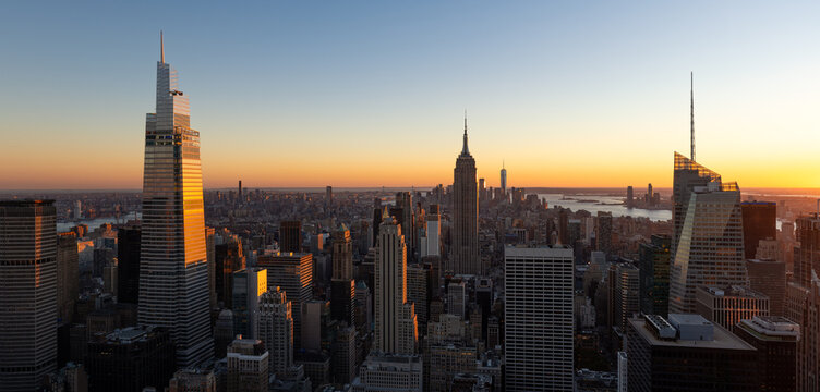 UNITED STATES, NEW YORK CITY, MANHATTAN. ELEVATED PANORAMIC SKYLINE VIEW OF THE SKYSCRAPERS OF MIDTOWN MANHATTAN ONE VANDERBILT ON THE LEFT AND EMPIRE STATE BUILDING AT CENTER AT SUNSET