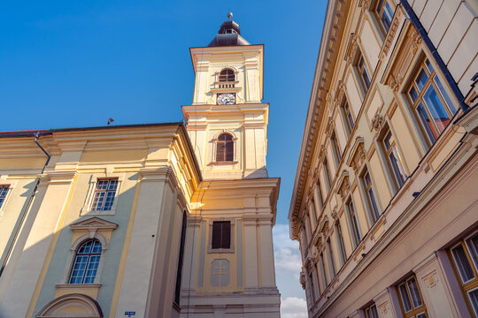 Low angle view of Holy Trinity Roman Catholic Church tower between historic buildings in Sibiu Romania.