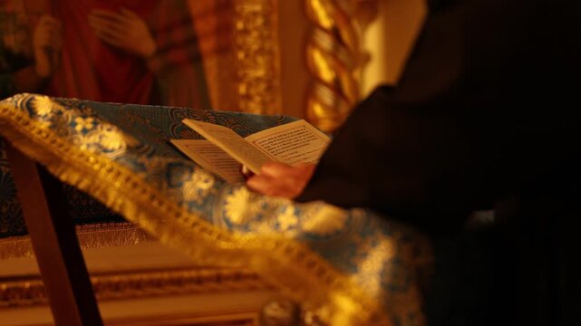 Hands holding open book on ornate lectern in warm gilded interior, subtle page and silhouette shifts, with book, hand, lectern, brocade detail, showing gold, blue, fringe, pattern context