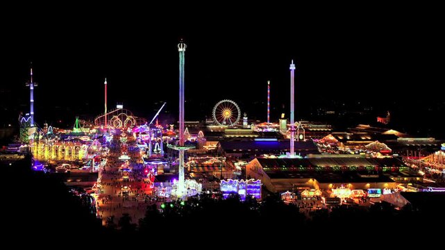 Aerial panorama of the oktoberfest in munich at night - world-famous folk festival in bavaria with colorful lighting, rides, roller coasters visitors and cozy beer tent atmosphere - Germany 