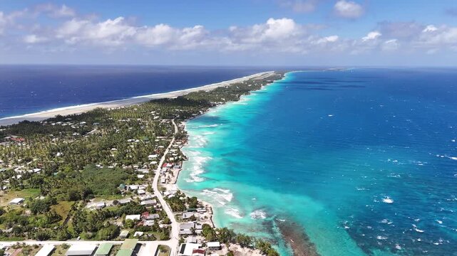 An aerial drone shot orbits clockwise over the narrow motu of Rangiroa Atoll, capturing Avatoru village, the lush palm canopy, and the vivid gradient of the turquoise lagoon