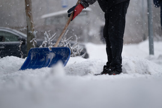 Person Shoveling Snow on City Sidewalk During Winter Snowfall