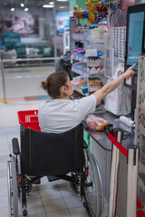 Obraz premium A Caucasian woman in a wheelchair pays for groceries at a self-checkout counter in a supermarket.