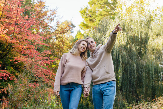 Young happy Caucasian couple in love holding hands and enjoying the moment during romantic walk on nature in the fall park. Autumn mood. Youth feelings and first love emotions concept.