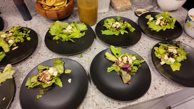 Chef Preparing Multiple Gourmet Green Salads for Event Catering on Black Plates