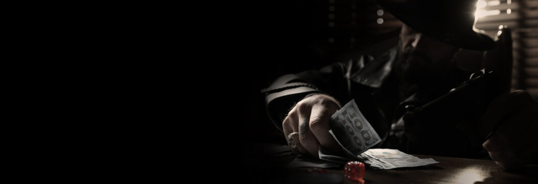 Mafia. Man with gun and dollar banknotes at wooden table in dark room, selective focus. Banner design with space for text