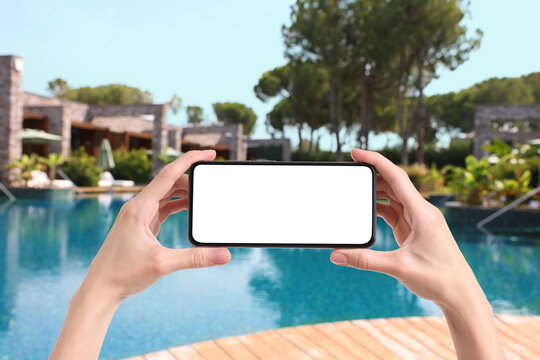 Woman holding mobile phone with blank screen on sea resort by swimming pool, closeup