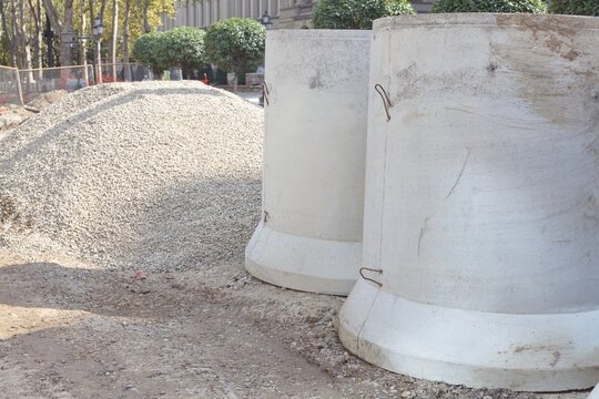 Precast concrete manhole rings and a pile of crushed gravel at an urban road reconstruction site
