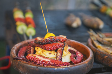 Grilled Octopus Tentacles. Close-up of grilled octopus tentacles with grilled food in rustic ceramic bowl at outdoor food stall. Mediterranean seafood candid scene, culinary and street food themes © svetlanais