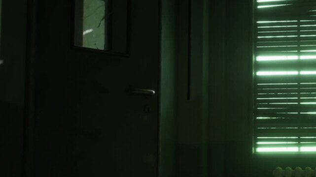 In a dimly lit room, a door stands slightly ajar, casting shadows that dance along the walls as green light filters through closed blinds, creating an eerie yet captivating atmosphere.