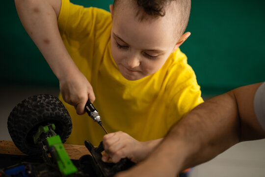 Young boy learning repair skills assisting father with toy car