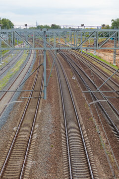 Multiple parallel steel railway tracks extend into the distance under overhead electrification gantries during a clear day in an industrial landscape.