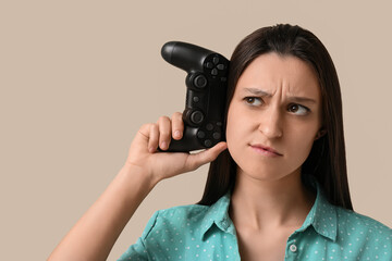 Gaming addiction and digital burnout, confused young woman holding a video game controller to her ear as if listening to technology © Pixel-Shot