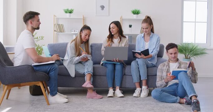 Portrait of a young cheerful people students group sitting on sofa in living room at home and studying indoors preparing for test together making notes discussing learning. 4k video.