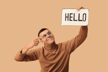 Handsome young man pointing at speech bubble with word HELLO on brown background © Pixel-Shot