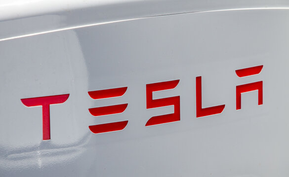 Close‑up of Tesla charging unit displaying red corporate lettering on white enclosure at contemporary electric‑vehicle charging site