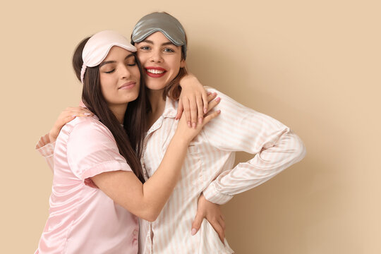 Female friends with sleeping masks hugging on beige background