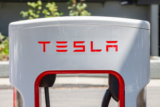 Close‑up of Tesla charging unit displaying red corporate lettering on white enclosure at contemporary electric‑vehicle charging site