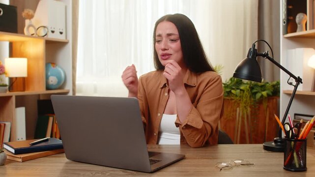 Young woman on home table looks at laptop error and feels upset after failed result during work at home. Adult girl on home table worries about rejection and shows stress and disappointment indoors.