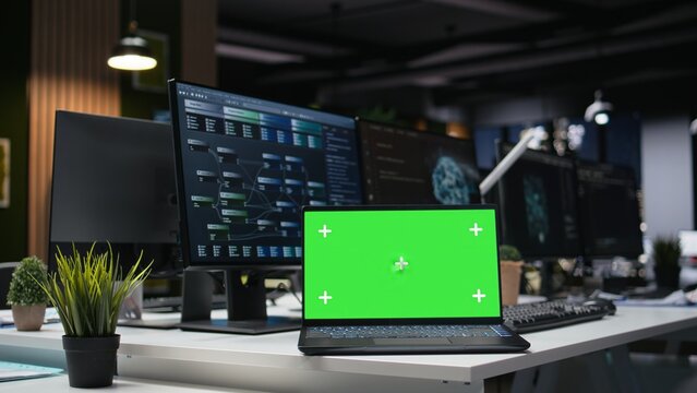 Green screen mockup laptop in an office is used to automate app development tasks with machine learning, while a chroma key notebook in an empty startup workplace accelerates feature implementation.
