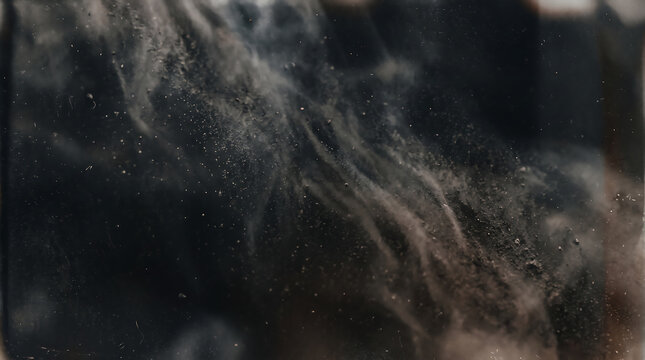 Close-up of black ash texture with fine particles and smoke-like swirls on dark background