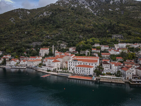 Perast coastal town with red roofs nestled against a lush green mountain on an overcast day