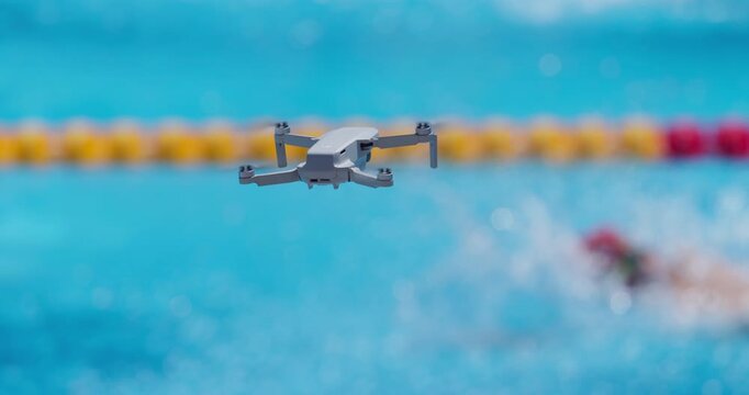 Small drone flying over swimming pool filming swimmer in action