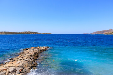 Fototapeta premium Calm blue sea meets rocky shore under clear sky