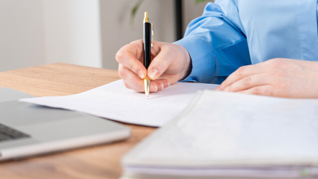 Close-up shows hands writing on paper with a pen