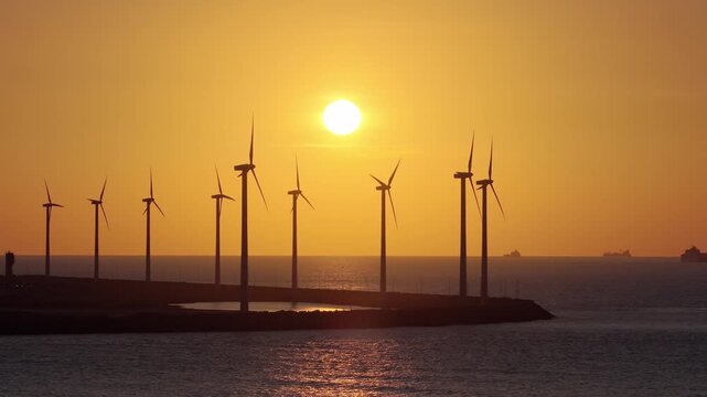 Drone view of wind turbines against a vibrant sunset. Silhouettes of wind turbines. Green renewable energy and wind farm technology at dusk.