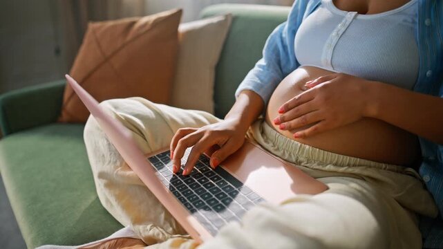 Belly closeup pregnant woman typing pink laptop. Expectant mom touching tummy.