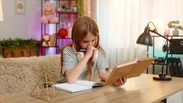 Young child girl sitting at table on home sofa looks sadly into school textbook struggling to understand the task. School kid holds head in confusion showing frustration and difficulty during homework