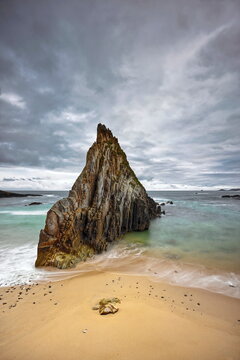 Sharp, central rocky islet midway along Playa de Mexota-A Mixota Beach, at rising tide in a cloudy yet spectacular spring sunrise. Asturias-Spain-010