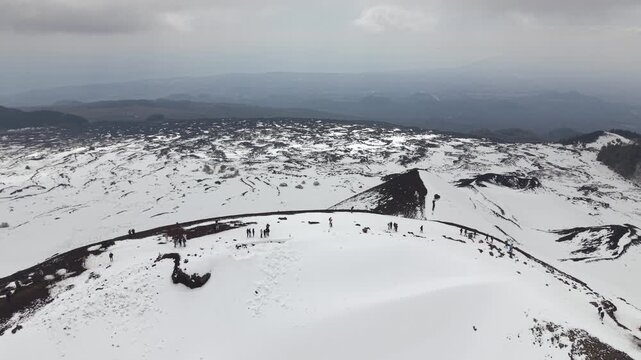 Cinematic drone shot of snowy Silvestri Craters on Mount Etna volcano, Italy. Aerial view of black volcanic rock and melting snow field during spring.