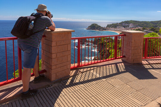 Photographer taking pictures from a viewpoint above the Mediterranean coastline and beach in Tossa de Mar, Costa Brava, Spain.