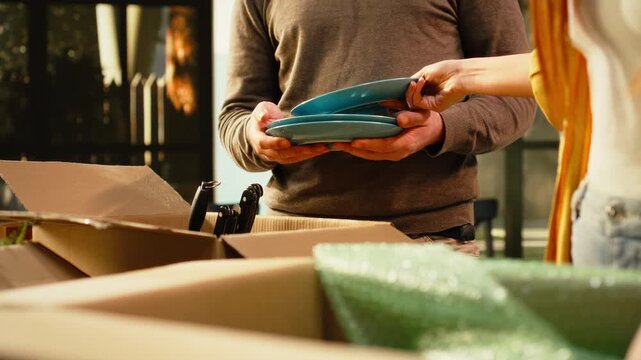 Close up of a man and woman unpacking home items wrapped in boxes while settling into their new house, arranging furniture and decorations after moving day during a major life event.