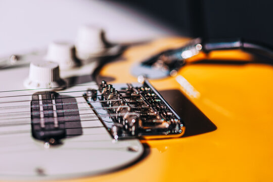 Electric guitar bridge, saddles, and tremolo arm in sharp detail. Guitar volume and tone knobs blur softly in the background