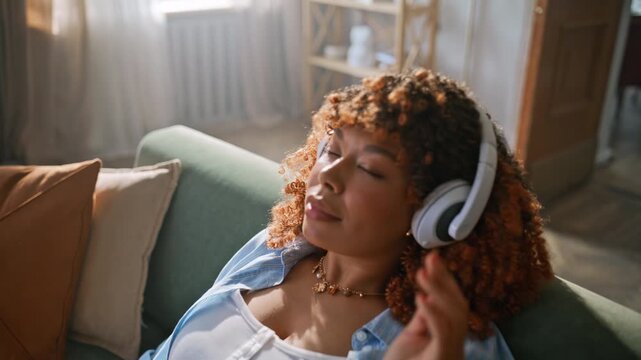 Pregnant woman listening music headphones home. Close up hands stroking belly.