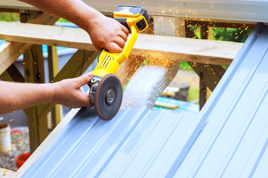 Worker uses power tool to cut metal sheet on construction site in sparks fly from cutting process.