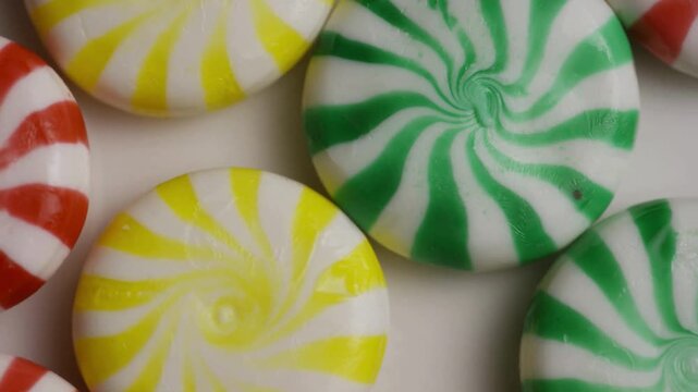 Assorted colorful round peppermint candies rotating on white surface