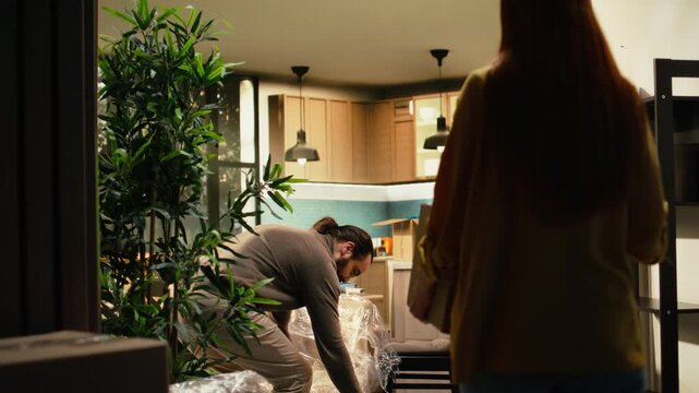 Young couple unboxing decorations in their new house, cherishing memories in a melancholy moment while redecorating their residence and enjoying a fresh start after relocation together on moving day.