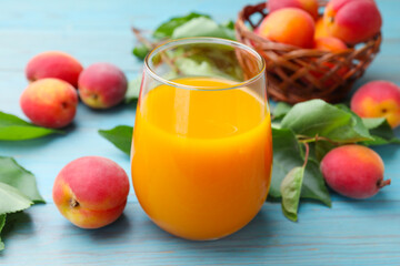 Apricot juice in glass, fresh fruits and leaves on light blue wooden table, closeup © New Africa