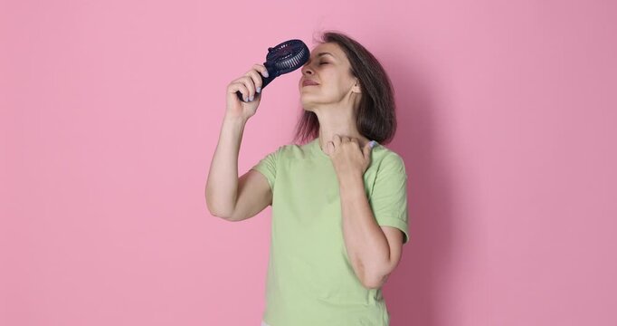 Smiling woman cooling down with portable mini fan on pink background