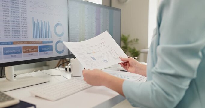 Accountant woman analyzing reports at computer. Financial dashboards on dual monitors guide review as she checks figures and paperwork in an office. Clear accounting and finance concept