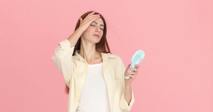 Woman cooling down with portable mini fan on pink background