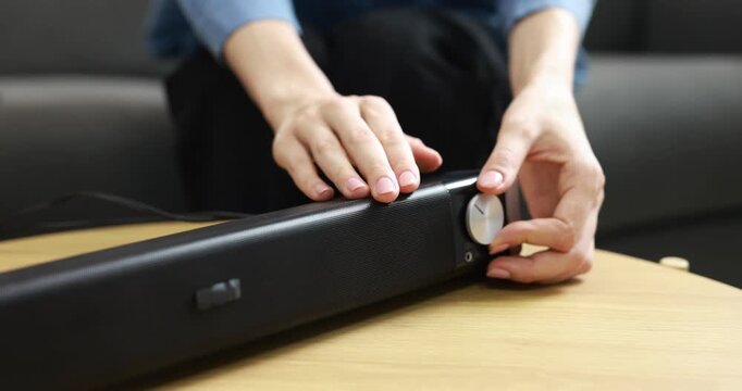 Woman adjusting volume on portable audio speaker at wooden table indoors, closeup